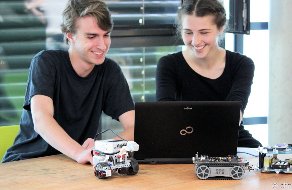 Schüler und Schülerin arbeiten am Computer, vor ihnen selbstgebaute Fahrzeuge aus Lego