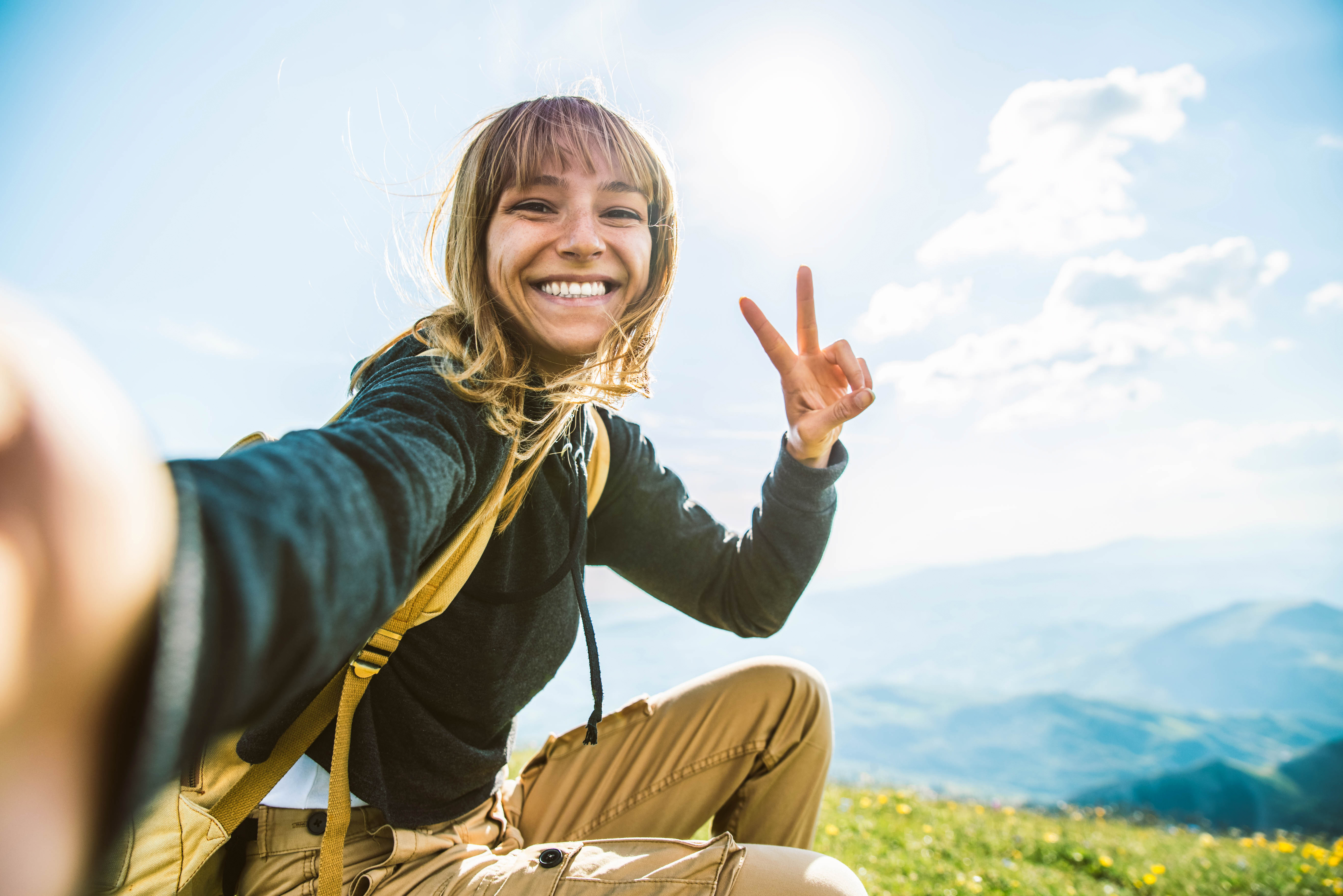 junge Frau in den Bergen, macht Selfie und grüßt in die Kamera